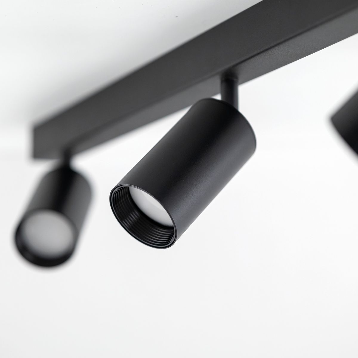 Lampa sufitowa Amis w kolorze czarnym z trzema reflektorami GU10. Reflektory umieszczone na prostokątnej, płaskiej podstawie, lekko skierowane w dół. Widok z dołu, podkreślający cylindryczny kształt lamp.