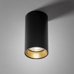 Czarna lampa sufitowa Amis z oprawą na jedną żarówkę GU10. Cylindryczny kształt, matowe wykończenie zewnętrzne oraz złote detale wewnątrz. Umieszczona frontalnie, montowana do sufitu, idealna do nowoczesnych wnętrz.