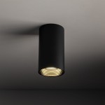 Lampa sufitowa Amis w kolorze czarnym z oprawą na żarówkę GU10. Posiada cylindryczny kształt i teksturowaną wewnętrzną powierzchnię. Ujęcie z dołu, ukazujące montaż do sufitu i emitowane światło. Prosta konstrukcja, idealna do nowoczesnych wnętrz.