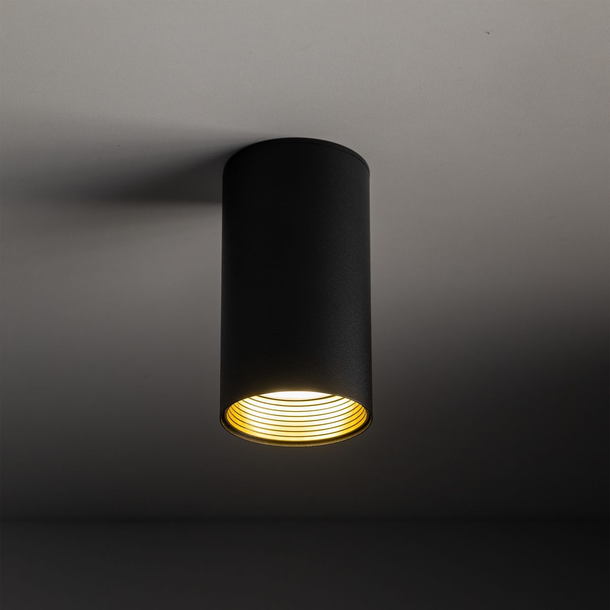 Czarna lampa sufitowa Amis z oprawą na jedną żarówkę GU10. Cylindryczny kształt, widoczne złote detale wewnątrz. Montowana na suficie, w minimalistycznym stylu, idealna do nowoczesnych wnętrz.