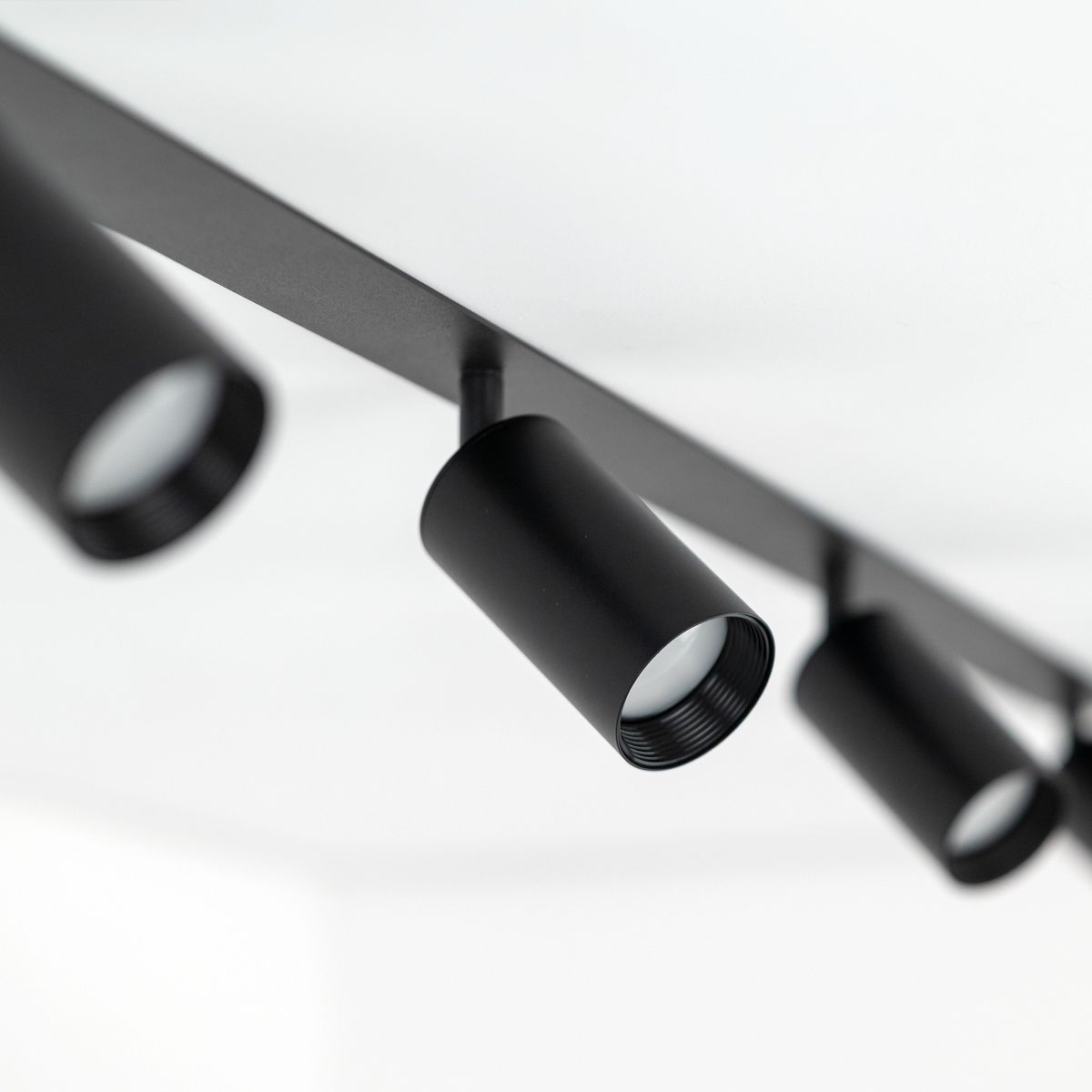 Czarna lampa sufitowa podtynkowa Amis z czterema reflektorami GU10. Ujęcie z bliska ukazuje cylindryczne oprawy świetlne zamocowane na prostokątnej podstawie. Całość na jasnym tle, co podkreśla minimalistyczny design.