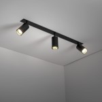 Lampa sufitowa podtynkowa Amis w kolorze czarnym z trzema reflektorami GU10, zamontowana na prostokątnej listwie. Reflektory są ustawione w różnych kierunkach, co umożliwia regulację oświetlenia. Tło jasne, gładkie.