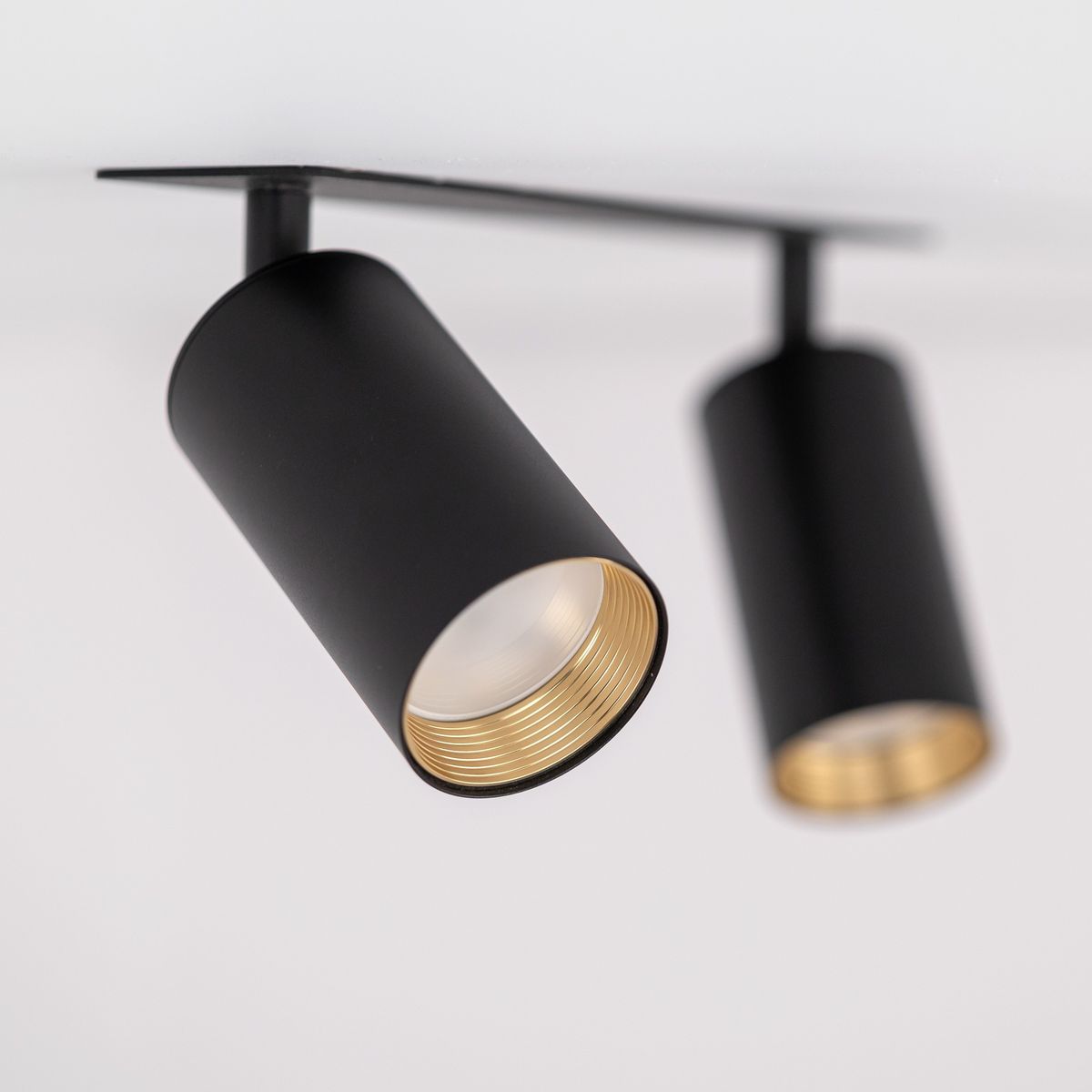 Lampa sufitowa podtynkowa Amis z dwoma reflektorami, kolor czarny. Cylindryczne oprawy z metalicznymi, złotymi wkładkami, zamontowane na prostokątnej podstawie. Ujęcie z dołu, pokazujące detale konstrukcji.