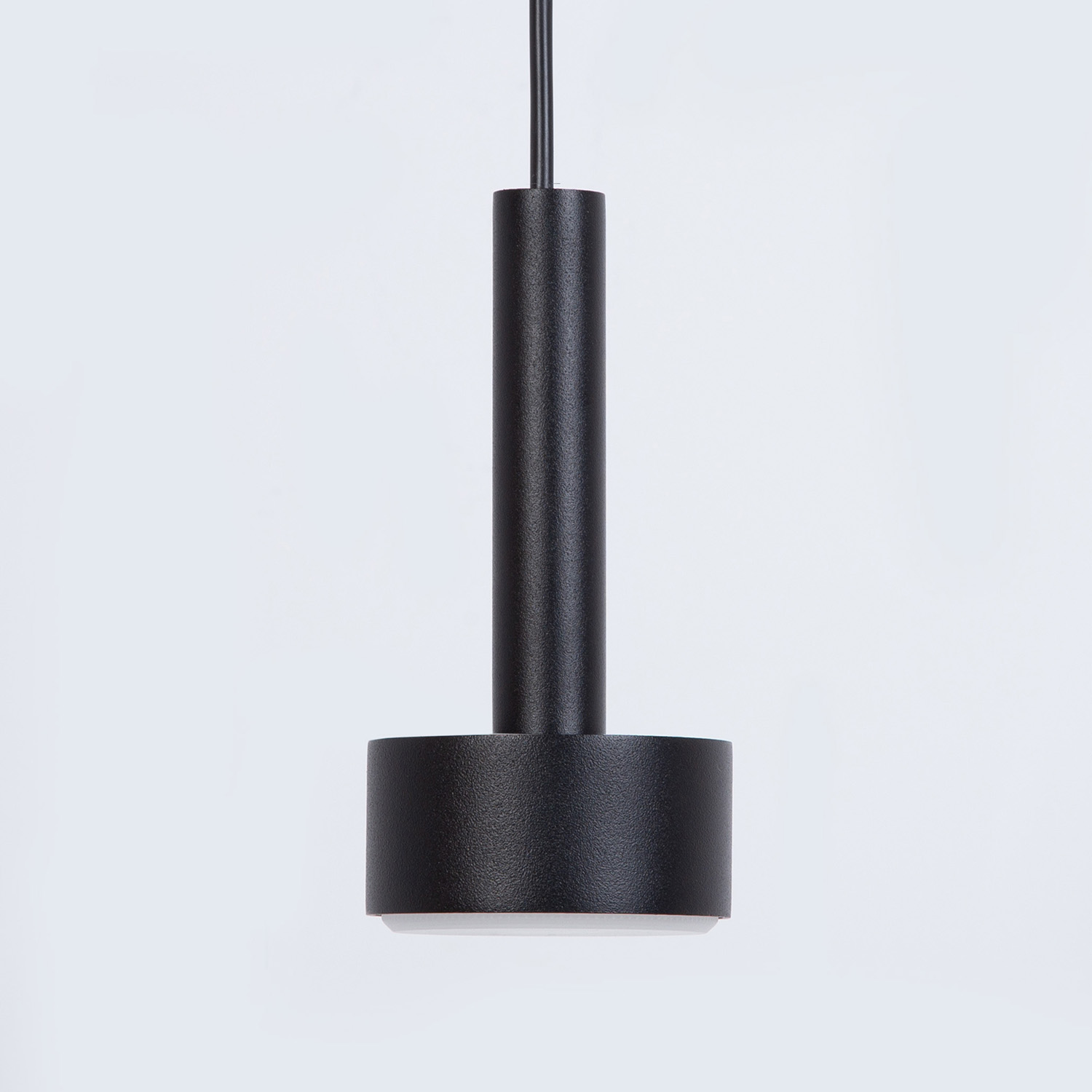 Lampa wisząca Stamp w kolorze czarnym, z metalowym korpusem o cylindrycznym kształcie. Posiada jeden uchwyt na żarówkę GX53, zawieszona na cienkim przewodzie, z prostym, nowoczesnym designem. Tło jasne, jednolite.