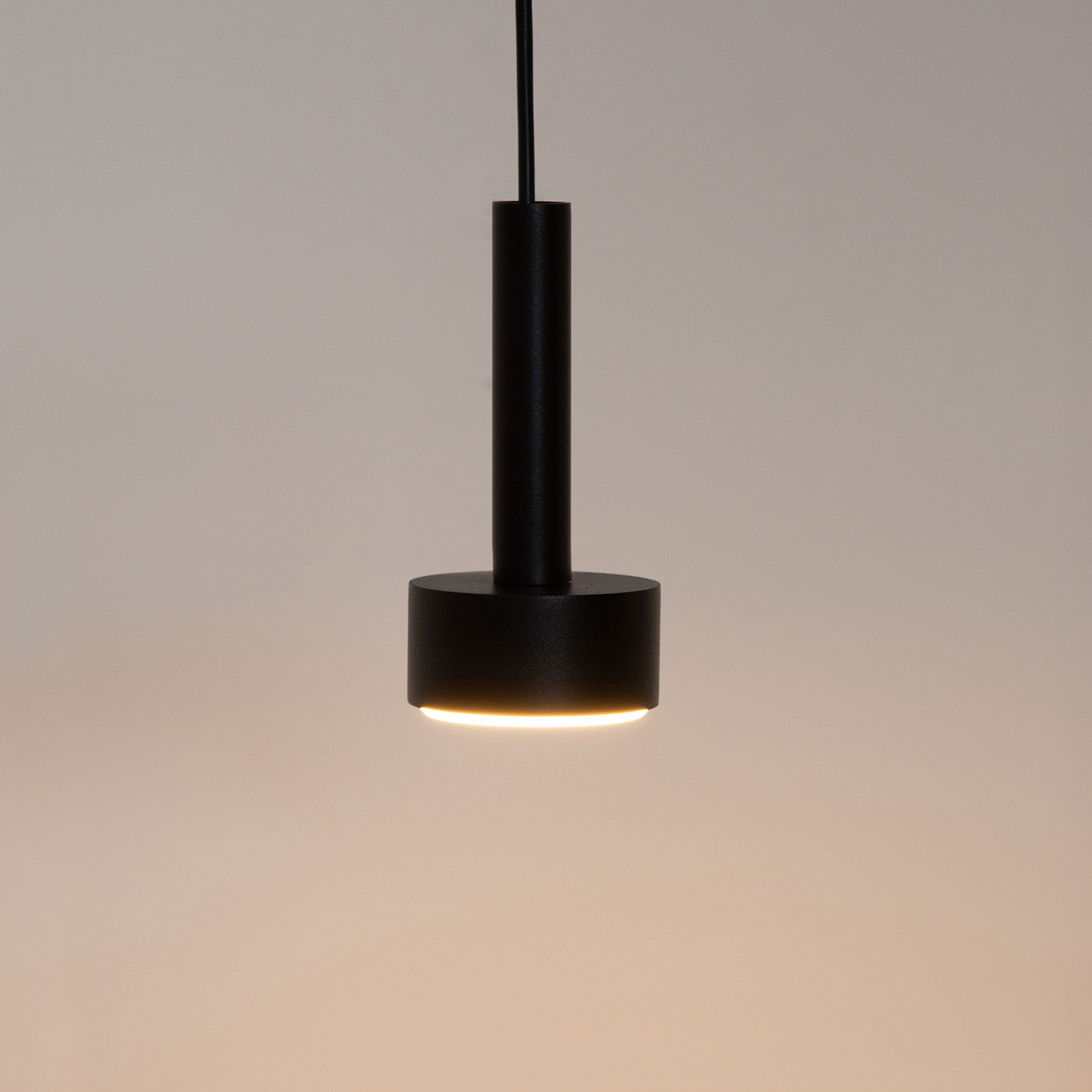 Lampa wisząca Stamp w kolorze czarnym z jedną oprawą GX53. Ma cylindryczny kształt z matowym wykończeniem. Zawieszona na cienkim przewodzie, emitująca ciepłe światło, idealna do nowoczesnych wnętrz.