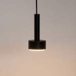 Lampa wisząca Stamp z dwoma gniazdami GX53 w kolorze czarnym, o cylindrycznym kształcie i matowej powierzchni. Produkt zawieszony na cienkim przewodzie, emitujący ciepłe światło z dolnej części klosza.