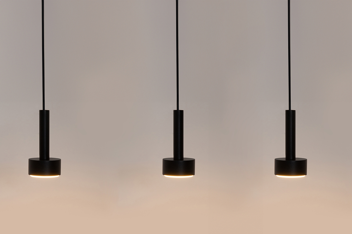 Czarna lampa wisząca Stamp z trzema źródłami światła GX53. Prosty, cylindryczny kształt z okrągłą podstawą. Zawieszona na cienkich linkach, w minimalistycznym stylu, idealna do nowoczesnych wnętrz.