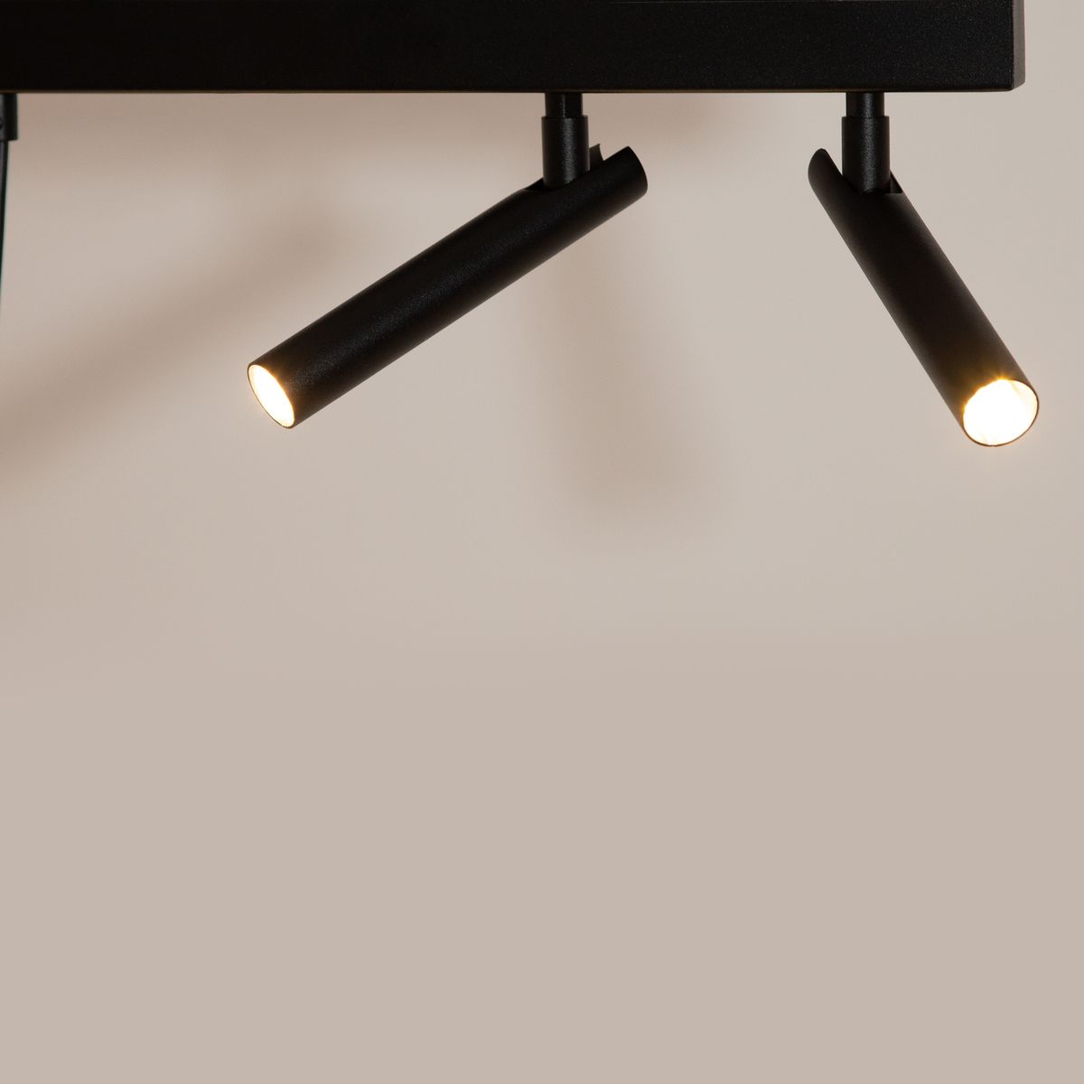 Lampa wisząca Stamp w kolorze czarnym z dwoma reflektorami w kształcie cylindrów. Reflektory są zamocowane na poziomej podstawie, emitując światło z dwóch źródeł G9. Tło w jasnym odcieniu podkreśla nowoczesny design lampy.