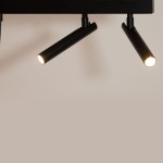 Lampa wisząca Stamp w kolorze czarnym z dwoma reflektorami w kształcie cylindrów. Reflektory są zamocowane na poziomej podstawie, emitując światło z dwóch źródeł G9. Tło w jasnym odcieniu podkreśla nowoczesny design lampy.