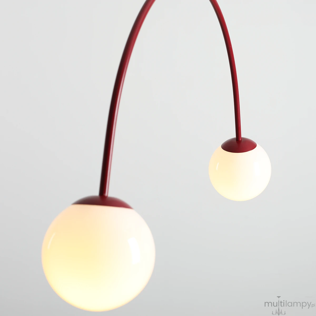 Lampa wisząca Una Red Wine z dwoma kulistymi kloszami w białym kolorze, zawieszona na elastycznym, czerwonym ramieniu. Klosze mają metalowe wykończenie u góry, całość nowoczesna i minimalistyczna, idealna do różnych aranżacji wnętrz.