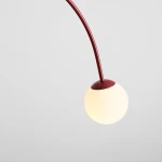 Lampa wisząca Una Red Wine z dwoma gniazdami E14, z elastycznym czerwonym ramieniem i okrągłą, matową oprawą w kolorze białym. Ujęcie z góry, ukazujące połączenie kolorów oraz minimalistyczny design. Tło w odcieniach szarości.