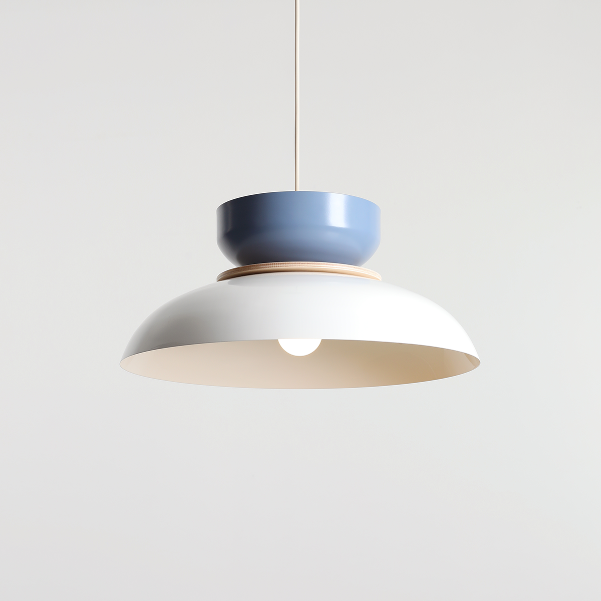 Lampa wisząca Aldo z białym kloszem i niebieską osłoną, z elementem drewnianym. Ujęcie frontalne, zawieszona na cienkim przewodzie. Kluczowe cechy to nowoczesny design i kolorystyka, idealna do nowoczesnych wnętrz.