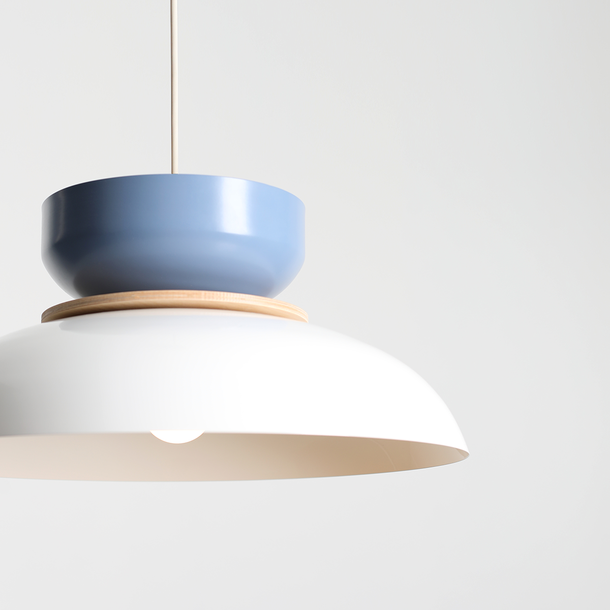 Lampa wisząca Aldo z jedną oprawą E27, z białym, półkulistym kloszem i niebieską, cylindryczną osłoną na górze. Elementy drewniane łączą obie części. Produkt zawieszony na cienkim przewodzie, na jednolitym tle.