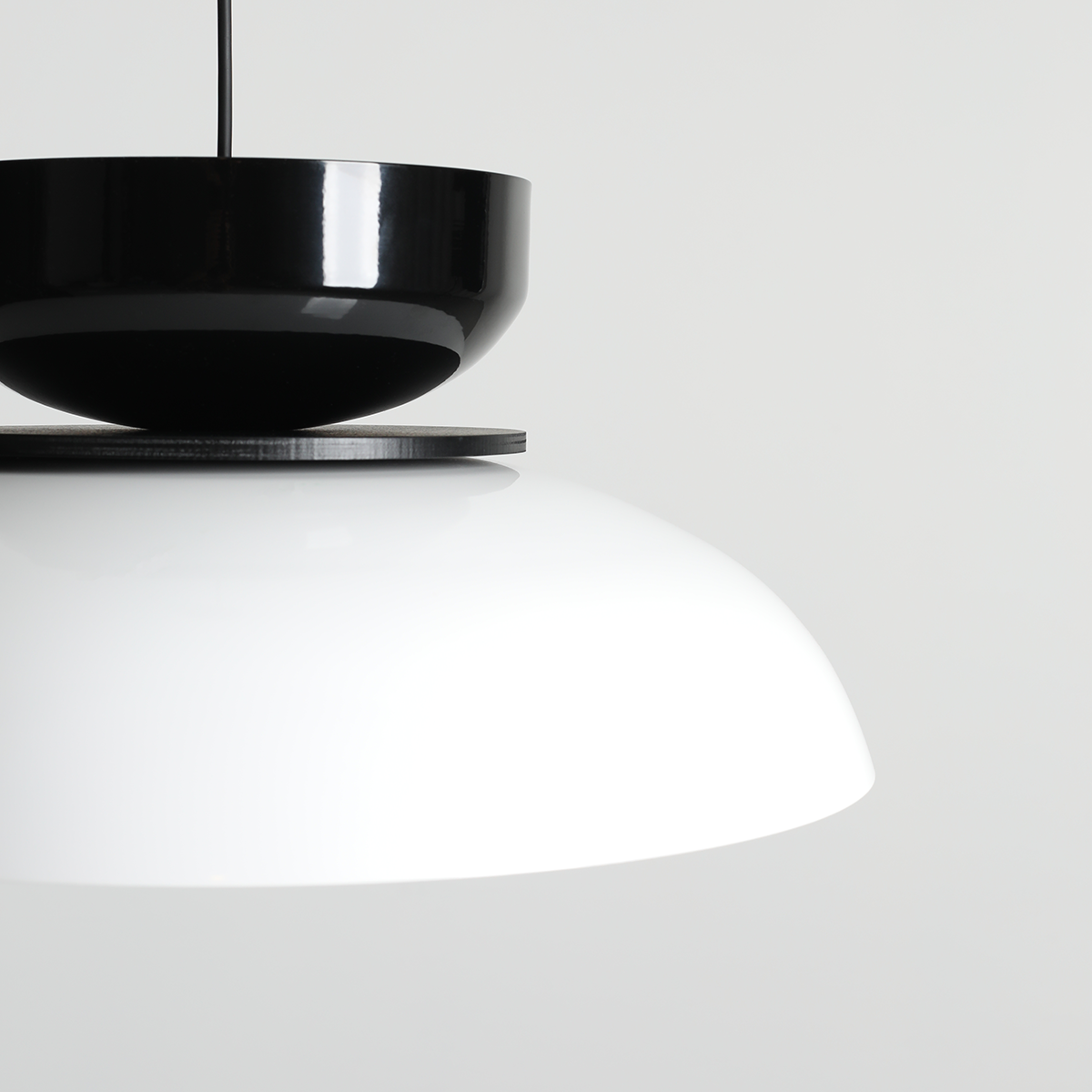 Lampa wisząca Aldo 1xE27 w kolorze białym i czarnym. Górna część w połyskującej czerni, dolna część z matowym białym kloszem w kształcie półkuli. Ujęcie z góry, eksponujące kontrasty kolorystyczne i formę.