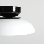 Lampa wisząca Aldo 1xE27 w kolorze białym i czarnym. Górna część w połyskującej czerni, dolna część z matowym białym kloszem w kształcie półkuli. Ujęcie z góry, eksponujące kontrasty kolorystyczne i formę.