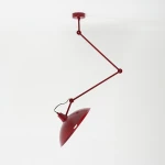 Lampa wisząca Melos 1xE27 w kolorze czerwonym, z metalowym kloszem o lekko zaokrąglonym kształcie. Uchwyt z ruchomymi ramionami, zamontowana na suficie. Prosta konstrukcja, na białym tle.