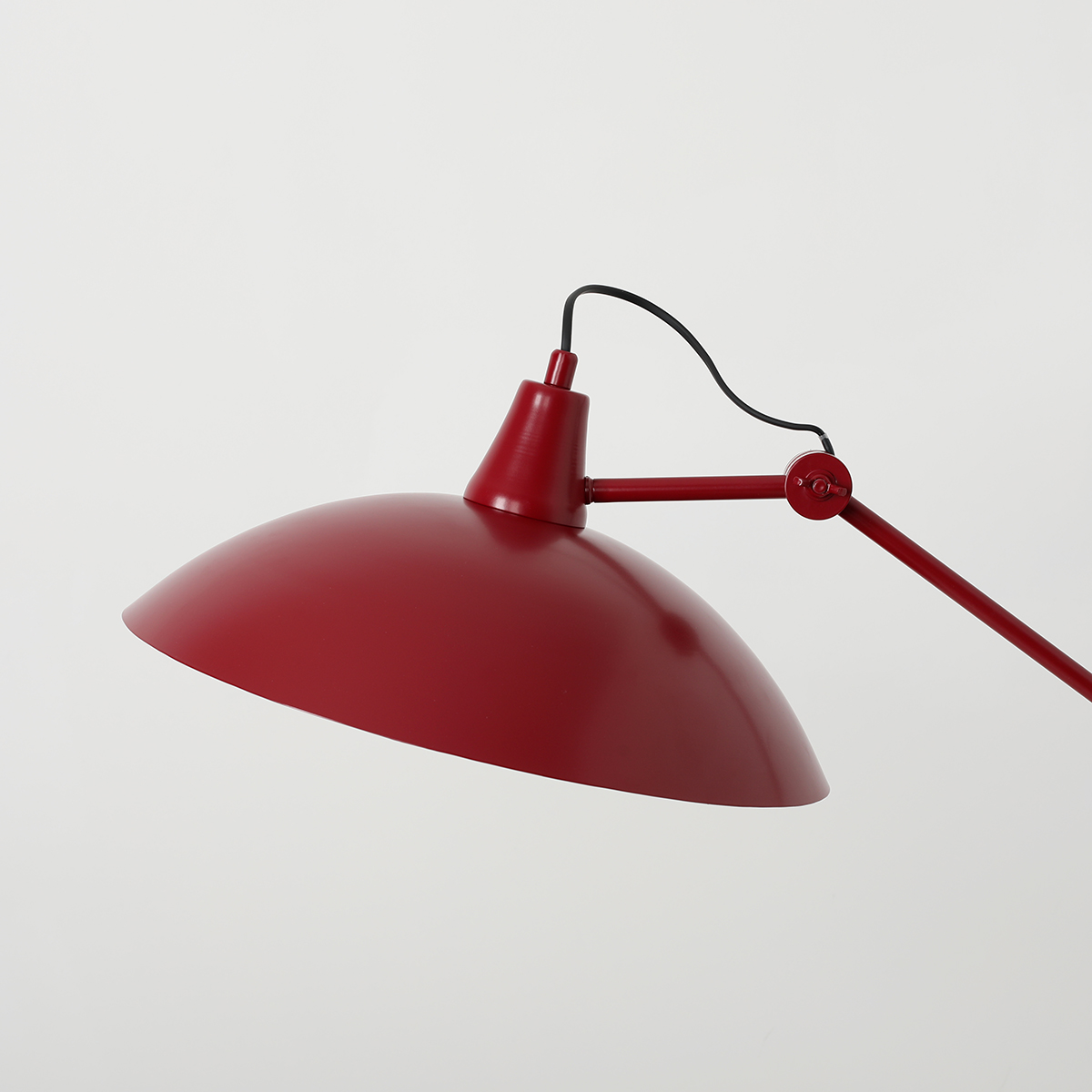 Lampa wisząca Melos w kolorze czerwonym z metalowym kloszem o półkulistym kształcie. Uchwyt i ramię w tym samym kolorze, z widocznym przewodem. Produkt zawieszony w górnej części, z możliwością regulacji kąta. Tło jasne, jednolite.