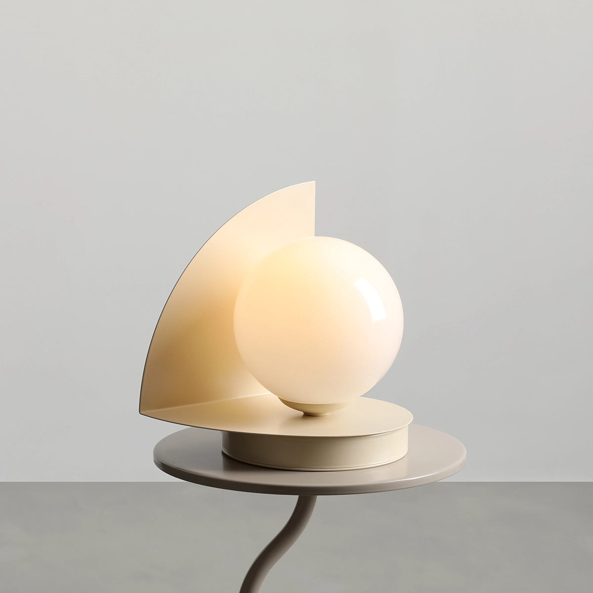 Lampa stołowa Loop Cream z kulistym kloszem w odcieniu kremowym, osadzona na okrągłej podstawie. Z boku znajduje się asymetryczny panel w tym samym kolorze, nadający nowoczesny charakter. Produkt ustawiony na płaskiej powierzchni.