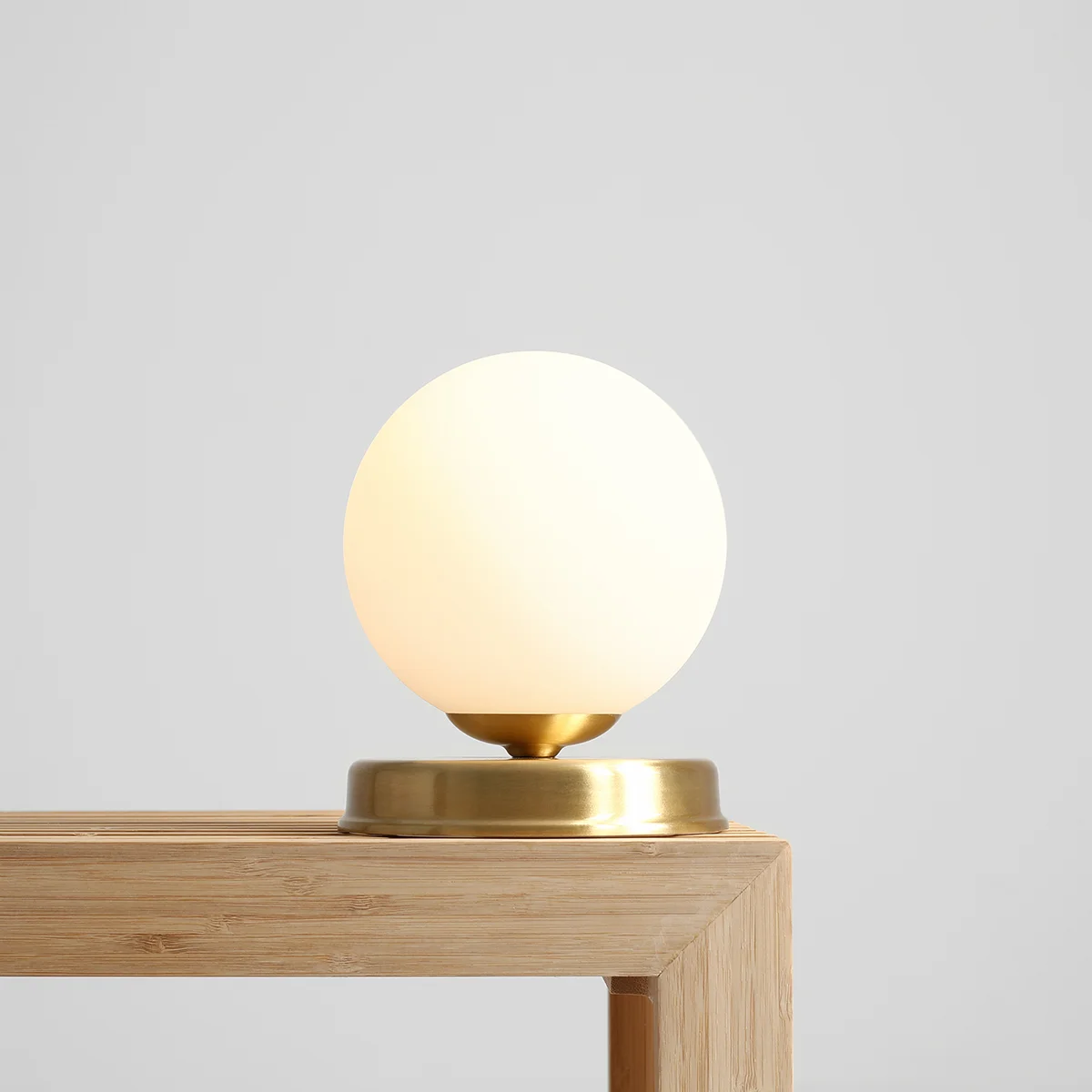Lampa stołowa Ball D14 z mosiężną podstawą, z okrągłym kloszem w kolorze mlecznym, umieszczona na drewnianym blacie. Widok z boku, podświetlająca elegancki design.