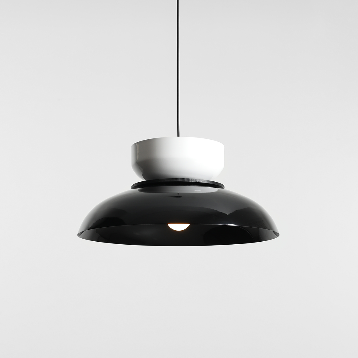 Lampa wisząca Aldo z jedną oprawą E27, w kolorze czarnym i białym. Górna część jest biała, dolna część ma kształt dużego, błyszczącego klosza w kolorze czarnym. Produkt zawieszony na cienkim przewodzie, na jednolitym tle.