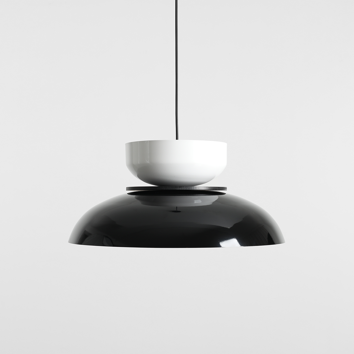 Lampa wisząca Aldo w kolorze czarnym i białym z jednym gniazdem E27. Posiada zaokrągloną, połyskującą czarną podstawę oraz białą, kulistą osłonę umieszczoną na górze. Zawieszona na cienkim czarnym przewodzie, na jednolitym tle.