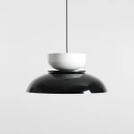 Lampa wisząca Aldo w kolorze czarnym i białym z jednym gniazdem E27. Posiada zaokrągloną, połyskującą czarną podstawę oraz białą, kulistą osłonę umieszczoną na górze. Zawieszona na cienkim czarnym przewodzie, na jednolitym tle.