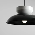 Lampa wisząca Aldo z kloszem w połyskującej czerni i białym elementem u góry. W kształcie stożka, z widocznym źródłem światła E27. Zawieszona na cienkim przewodzie, na jednolitym, jasnym tle.
