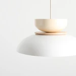 Lampa wisząca Aldo 1xE27 w kolorze białym i kremowym. Posiada dużą, półkulistą, białą osłonę oraz kremową, okrągłą górę z drewnianym elementem. Ujęcie z boku, na białym tle, ukazujące detale i konstrukcję lampy.
