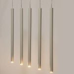 Sopel lampa wisząca w kolorze szarym beżowym, składająca się z pięciu długich, cylindrycznych elementów z delikatnym podświetleniem na końcach, zawieszona na cienkich przewodach. Idealna do nowoczesnych wnętrz.
