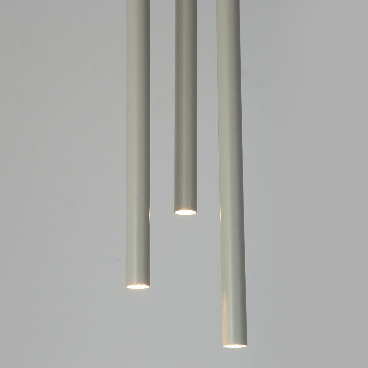 Lampa wisząca Sopel 3xG9 w kolorze szarym beżowym, składająca się z trzech długich, cylindrycznych elementów. Widoczne źródła światła na końcach lampy, zawieszona w pozycji pionowej na gładkim tle.