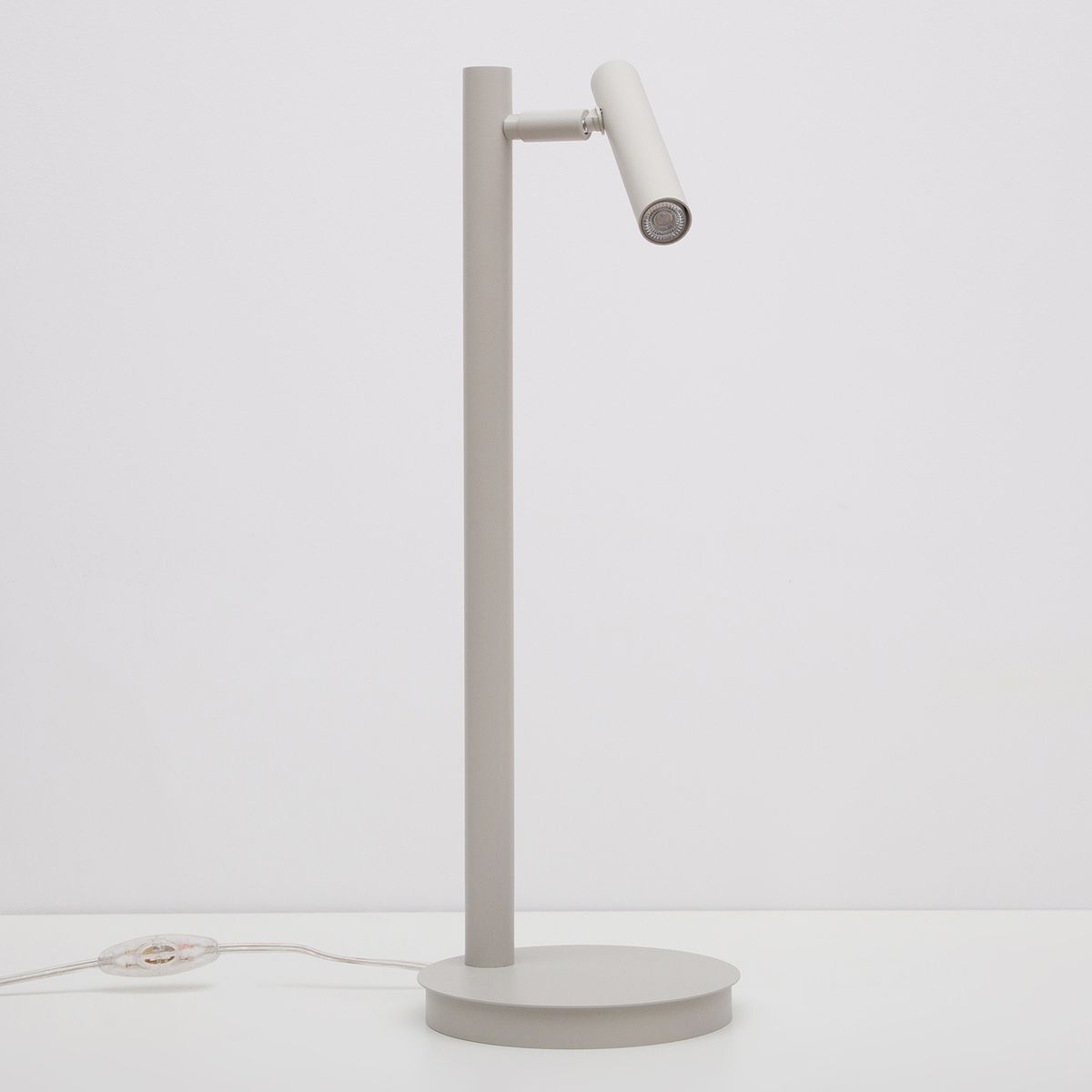 Lampka stołowa Sopel w kolorze szarym beżowym, z okrągłą podstawą i prostą, pionową nogą. Zwrotna głowica z miejscem na żarówkę G9. Kabel z przełącznikiem widoczny przy podstawie. Produkt na jednolitym tle.