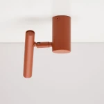 Lampa sufitowa typu spot Sopel Krótki w kolorze ceglastym. Posiada cylindryczne mocowanie i wydłużoną, ruchomą część emitującą światło. Produkt zamontowany na białym suficie, widoczny z boku.