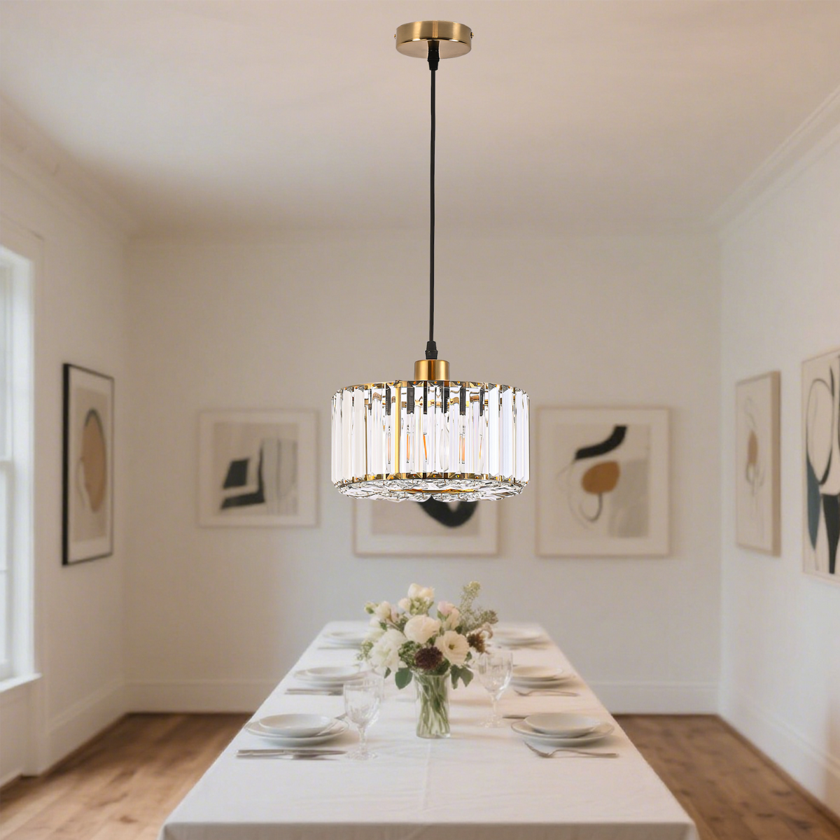 Lampa wisząca Vetro LP-2910/1P GD w kolorze złotym, okrągła, z przezroczystymi kryształkami, zawieszona na czarnym przewodzie. Produkt umieszczony w jasnym wnętrzu z białym stołem i dekoracją kwiatową.