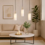 Lampa wisząca Vesta 3xE27 w kolorze złotym i białym z trzema cylindrycznymi kloszami, zawieszona na czarnych przewodach. W tle widoczny jasny salon z kanapą, okrągłym stolikiem, świecami i rośliną.