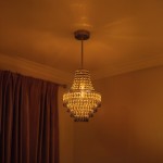 Lampa wisząca Gemma 1xE27 w kolorze chromu, o kształcie stożkowym, zdobiona kryształkami. Zawieszona na cienkim kabelku, emitująca ciepłe światło w przytulnym wnętrzu, z brązowymi zasłonami w tle.