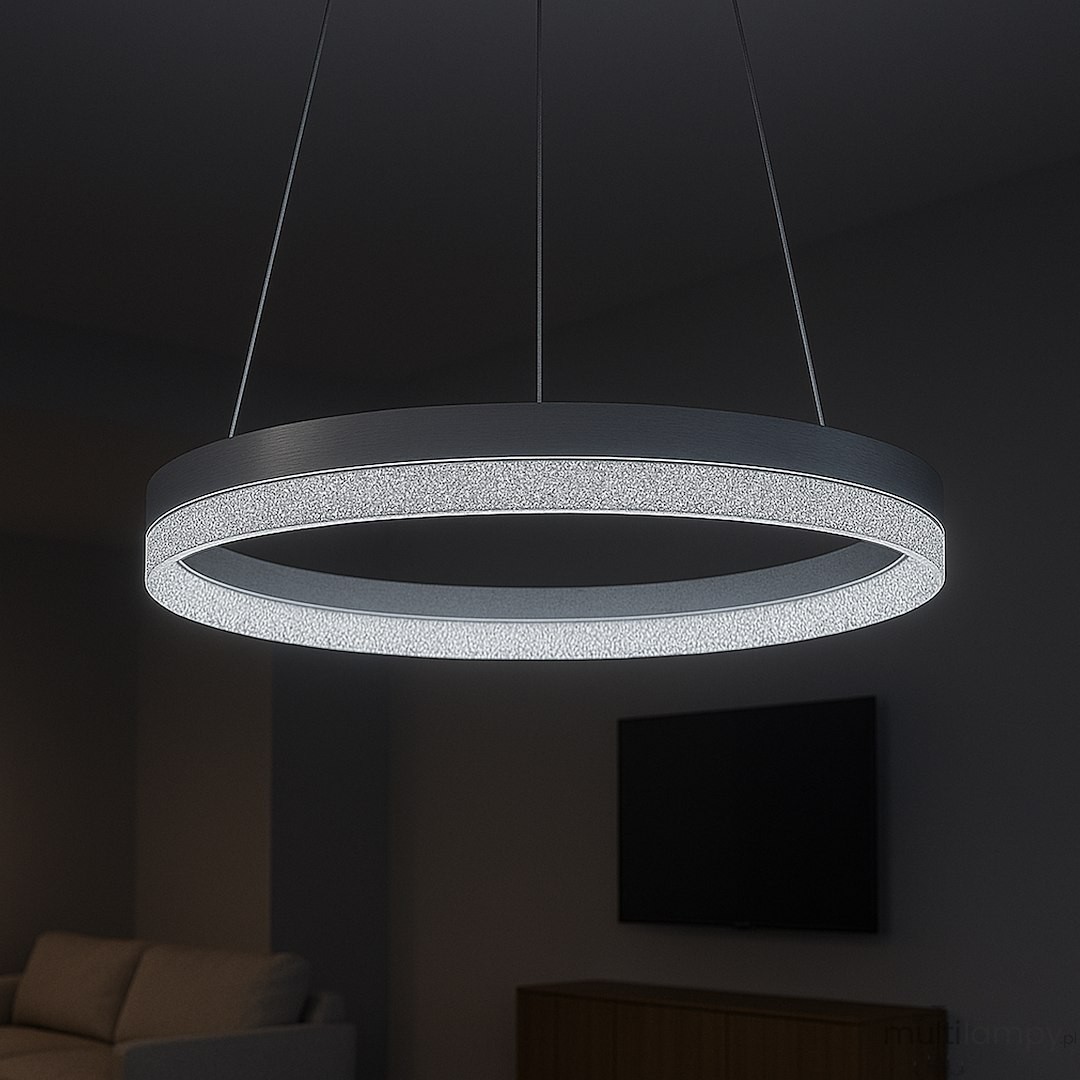 Lampa wisząca LED Gala 25W 4000K w srebrnym kolorze, o okrągłym kształcie. Zawieszona na cienkich linkach, emituje jasne, białe światło, z dekoracyjnym elementem wzdłuż krawędzi. Tło ciemne, w tle widoczny telewizor i sofa.