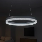 Lampa wisząca LED Gala 25W 4000K w srebrnym kolorze, o okrągłym kształcie. Zawieszona na cienkich linkach, emituje jasne, białe światło, z dekoracyjnym elementem wzdłuż krawędzi. Tło ciemne, w tle widoczny telewizor i sofa.