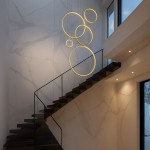 Lampa wisząca LED Saturno o mocy 100W, kolor złoty, składająca się z kilku okrągłych pierścieni. Zawieszona nad schodami w nowoczesnym wnętrzu, na tle jasnej ściany z marmurowym wzorem.