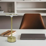 Lampa stołowa LED Tavolo 2,5W CCT w kolorze złotym, z okrągłą podstawą i smukłym stelażem. Ujęcie frontalne na biurku obok laptopa i notesu, na tle jasnej aranżacji wnętrza.