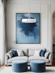 Lampa wisząca Doretto Satin w kolorze srebrnym, z niklowanym wykończeniem, z sześcioma miejscami na żarówki E27. Zawieszona centralnie nad szarym sofą z poduszkami na tle niebieskiego obrazu i jasnych ścian.