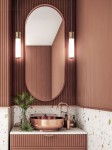 Lampa wisząca LED Omi I Gold 10W 3000K w kolorze złotym, zamontowana na ciemnoróżowej ścianie. Produkt o cylindrycznym kształcie z przezroczystym kloszem, zawieszony na czarnym przewodzie, idealny do nowoczesnych wnętrz.