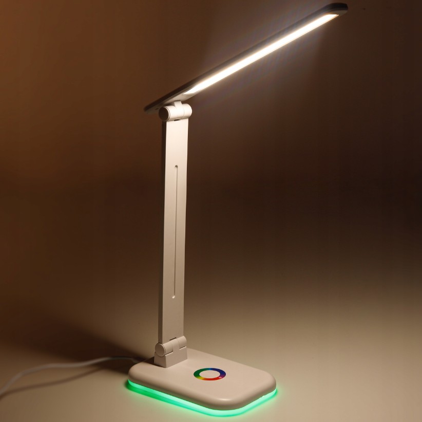 Biała lampka biurkowa Alma LED 12W/CCT z regulowanym ramieniem. U podstawy znajduje się kolorowy przycisk z podświetleniem RGB. Kąt ujęcia z boku, pokazujący nowoczesny design i funkcjonalność lampy.