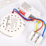 Plafon Luvo D29,5 w kolorze czarnym z czujnikiem ruchu. Widać elementy instalacyjne, w tym zasilacz LED z oznaczeniem, przewody w kolorach: niebieskim, czerwonym, żółtym i brązowym. Produkt montowany sufitowo, kwadratowy kształt.