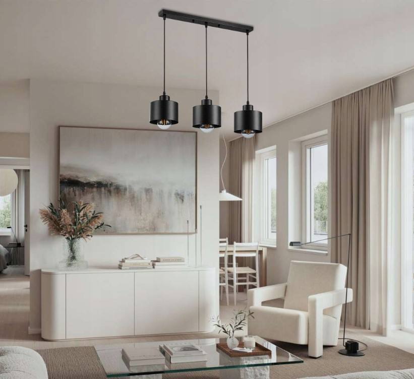 Lampa wisząca Elza w kolorze czarnym z trzema źródłami światła E27, zawieszona na prostokątnej podstawie. Wisi w nowoczesnym wnętrzu z jasnymi ścianami, dużymi oknami i minimalistycznymi meblami.