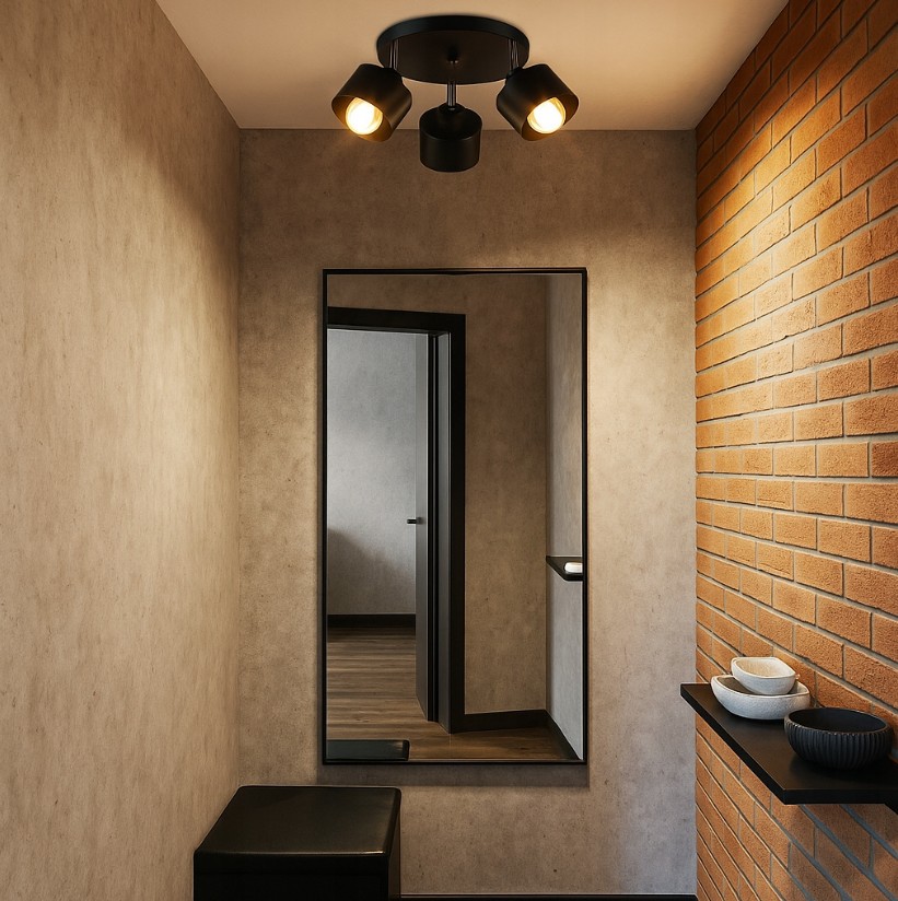 Okrągła lampa sufitowa Elza w kolorze czarnym z trzema punktami świetlnymi na ruchomych ramionach, zamontowana na gładkim suficie. W tle widoczna ceglana ściana oraz lustro w prostokątnej ramie.
