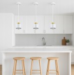 Lampa wisząca Elza 1xE27 w kolorze białym i złotym, z okrągłym kloszem, zawieszona na białym przewodzie. Widoczna w nowoczesnej kuchni, nad białym blatem, obok trzech drewnianych stołków barowych.