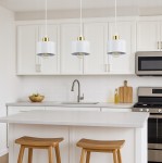 Lampa wisząca Elza z trzema oprawami E27 w kolorze białym i złotym, zawieszona nad blatem kuchennym. Stworzona z metalowych kloszy, z żarówkami, w nowoczesnym, minimalistycznym stylu. Otoczenie kuchenne z białymi szafkami i drewnianymi stołkami.