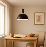 Czarna lampa wisząca Koko z oprawą z matowego metalu, o kulistym kształcie, zawieszona na cienkim przewodzie. Lampa umieszczona nad drewnianym stołem w jasnym wnętrzu, obok filiżanki i miski z owocami.