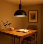 Czarna lampa wisząca Koko z jednym gniazdem E27, umieszczona nad drewnianym stołem. Lampa ma okrągły klosz i metalowy uchwyt. W tle widoczna ściana z obrazem oraz dekoracyjna roślina w wazonie. Oświetlenie tworzy przytulną atmosferę.