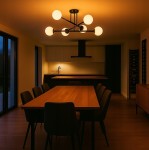 Czarna lampa sufitowa Bali z sześcioma miejscami na żarówki E27, w nowoczesnym stylu, zamontowana nad drewnianym stołem w kuchni. Oświetlenie tworzy ciepłą atmosferę w minimalistycznym wnętrzu z jasnymi i ciemnymi akcentami.